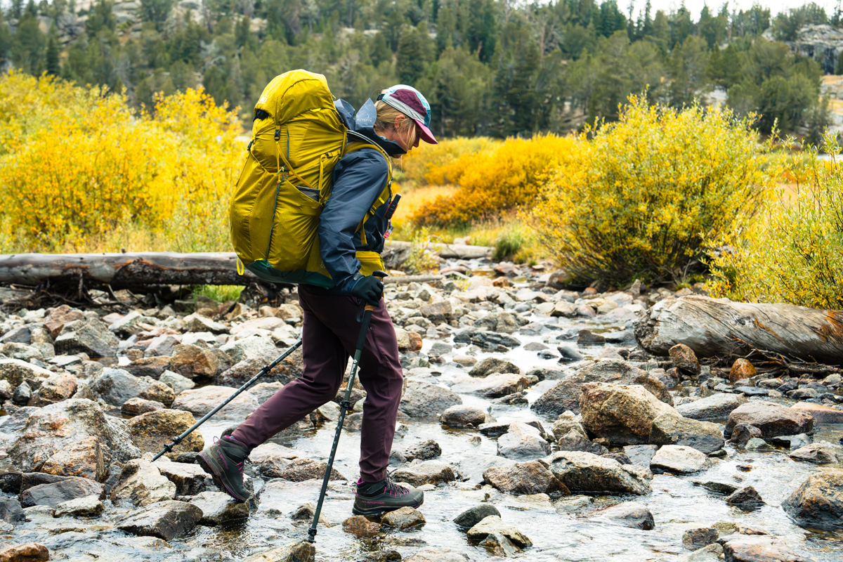 A hiker crosses a shallow stream while yellow fall foliage is in bloom.