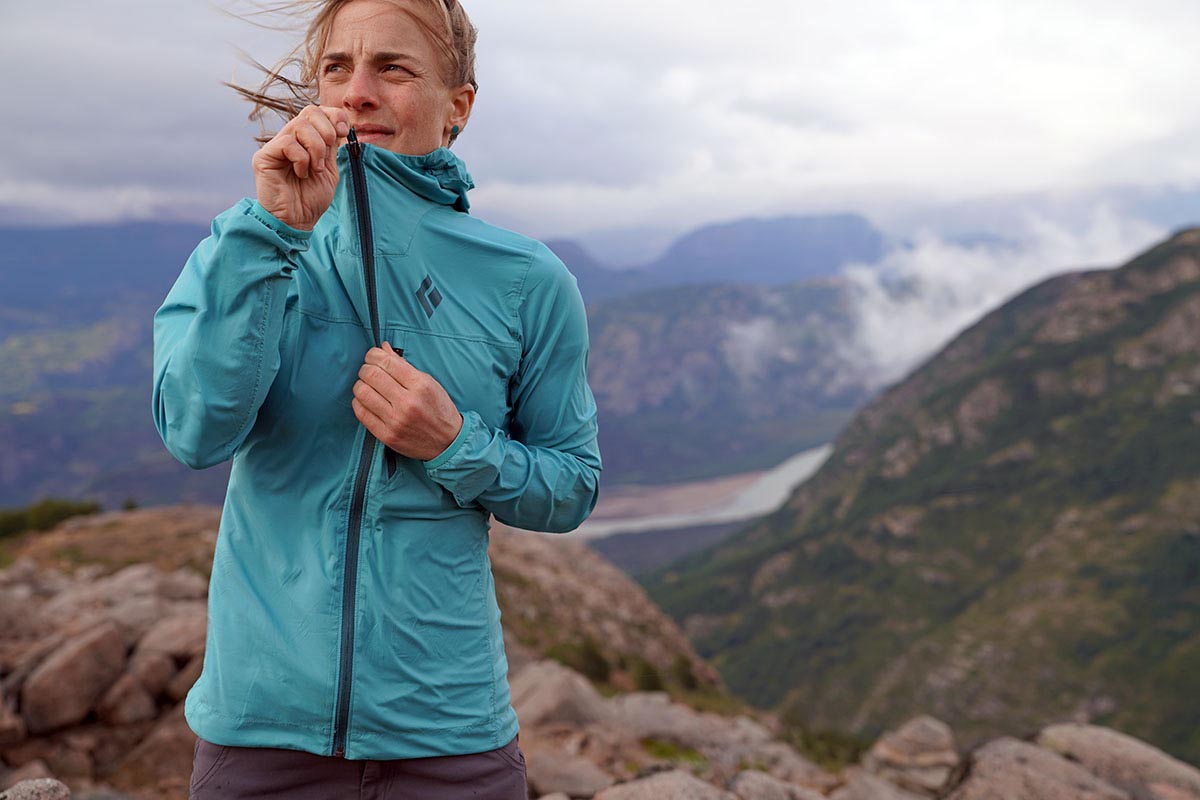 A woman zips a windjacket up against a strong mountain wind.